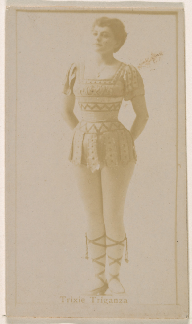 Ein altes Foto einer Frau in einem hellfarbenen gemusterten Badeanzug, mit ihrem Haar zu einem Knoten gebunden, die direkt in die Kamera posiert und leicht lächelt.