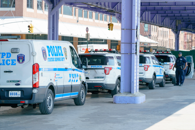 Eine Gruppe von Streifenwagen steht am Straßenrand einer Stadtstraße mit einer Person in der Nähe, Gebäude, Pfosten, Verkehrszeichen und eine Brücke im Hintergrund.