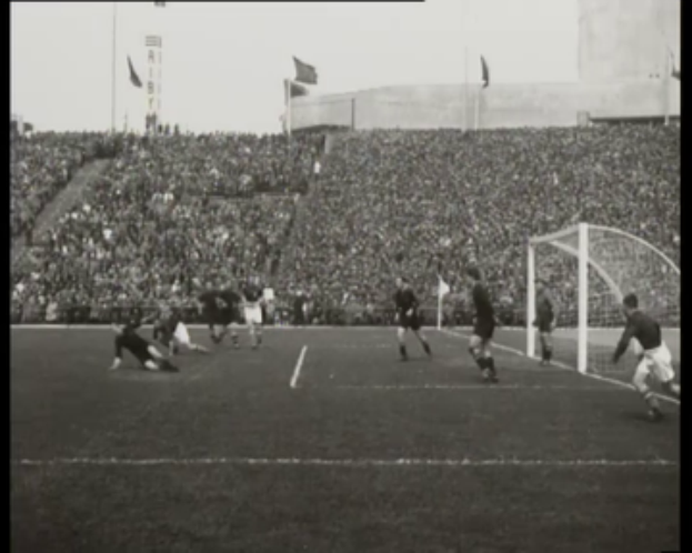 Ein Schwarz-Weiß-Foto eines Fußballspiels im Stadion, mit Spielern auf dem Feld und einem Torpfosten auf der rechten Seite, Zuschauern in den Rängen, Fahnen und einem klaren Himmel, mit Text oben und unten, der "1958-1958 WM-Finale - Manchester United v Liverpool" lautet.