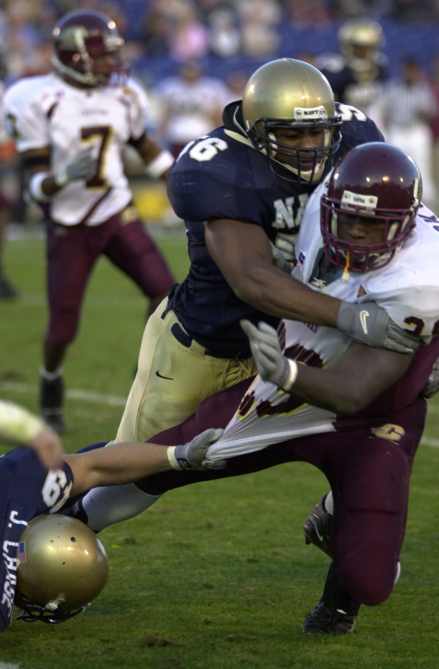 Zwei Fussballspieler in Helmen und Uniformen kollidieren auf dem Feld, während andere zuschauen.