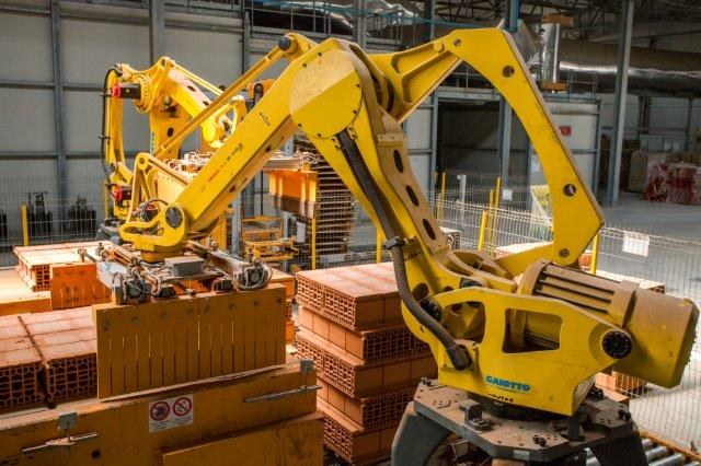 Großes Industriegelände mit gestapelten Kisten, Kränen, Zäunen, Pfählen und einer fernen Wand in einer automatisierten Fertigungsumgebung.