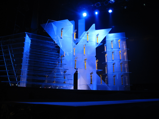 Eine Bühne für eine Preisverleihung mit dunklem Hintergrund, beleuchtet von ein paar Lichtern und verschiedenen Gegenständen, die mit dem Event in Verbindung stehen.