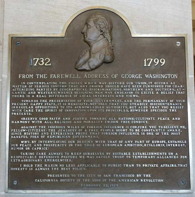 Plaque an einer Gebäudeseite mit Text "Aus der Abschiedsrede von George Washington" und einem zentralen geschnitzten menschlichen Gesicht.