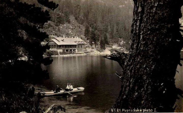 Ein Schwarz-Weiß-Foto von zwei Menschen in einem Kanu auf einem See, mit Paddeln in der Hand, umgeben von Bäumen und einem Haus im Hintergrund, aufgenommen in Popradskie, Polen, in den 1920er Jahren.