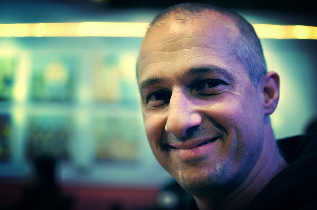 Ein Mann in einem schwarzen Kleid lacht, mit einem unscharfen Hintergrund, der undeutliche Lichter zeigt.