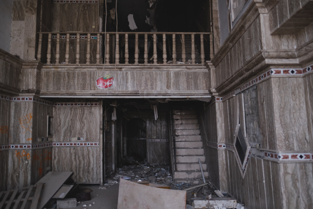 Ein altes Gebäudeinnere mit Schutt auf dem Boden, darunter hölzerne Gegenstände, Treppen, Geländer, Wände, Fenster und andere Gegenstände.