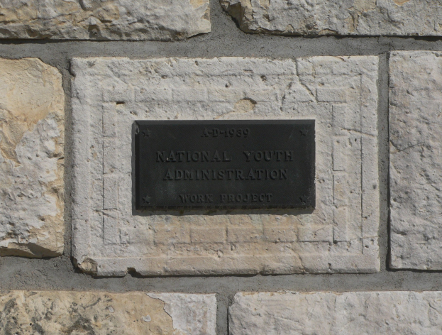 Steinwand mit einem rechteckigen schwarzen Schild, auf dem in weißer, fetter, zentrierter Schrift "Nationales Jugendamt" steht.