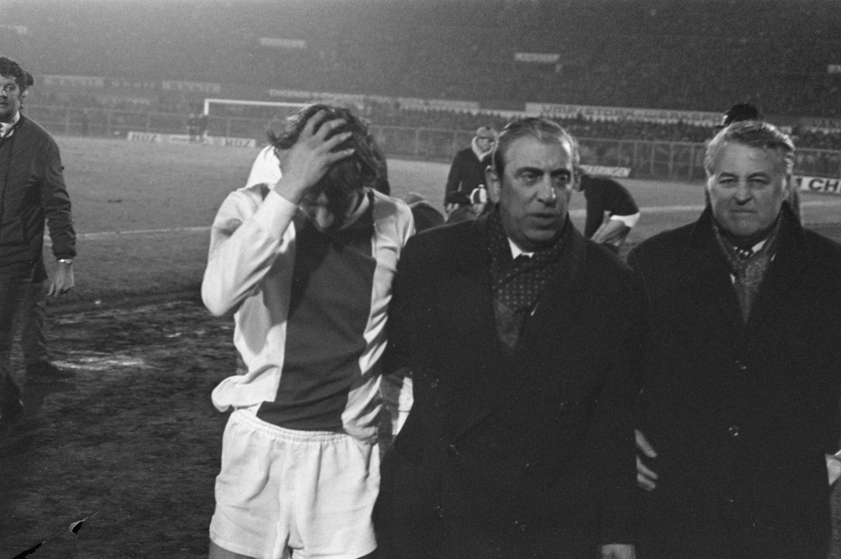 Schwarzes und weißes Bild von Männern in Not auf einem Fussballfeld mit einem Stadion im Hintergrund, wahrscheinlich nach einem Matchsieg.