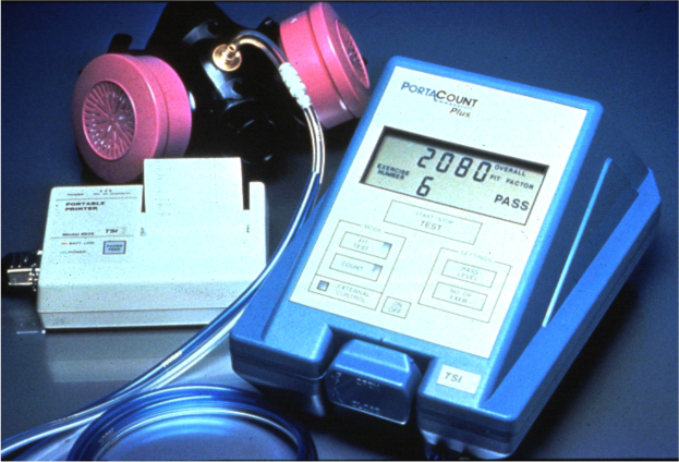 Eine Gasmask auf einem Tisch neben einem elektronischen Gasdetektionsgerät mit einem angeschlossenen Kabel.