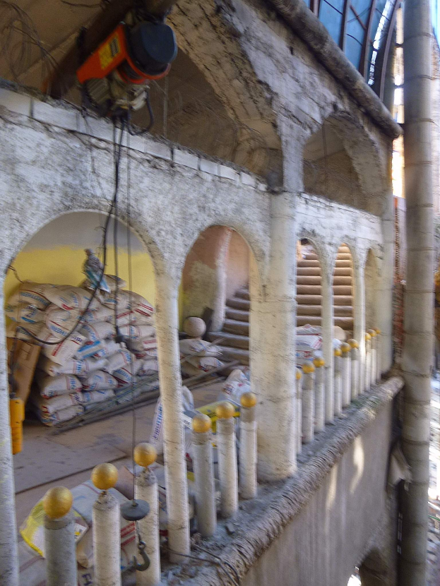 Altes Gebäude mit Bögen und Säulen wird renoviert, zeigt verstreute Werkzeuge, Materialien und Gegenstände, darunter eine Maschine und Drähte oben und Gegenstände am Boden.