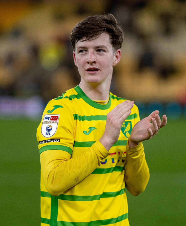 Ein junger Mann in einem gelb-grünen T-Shirt klatscht auf einem Fußballfeld in die Hände, mit einem unscharfen Hintergrund, der seine freudige Reaktion betont.