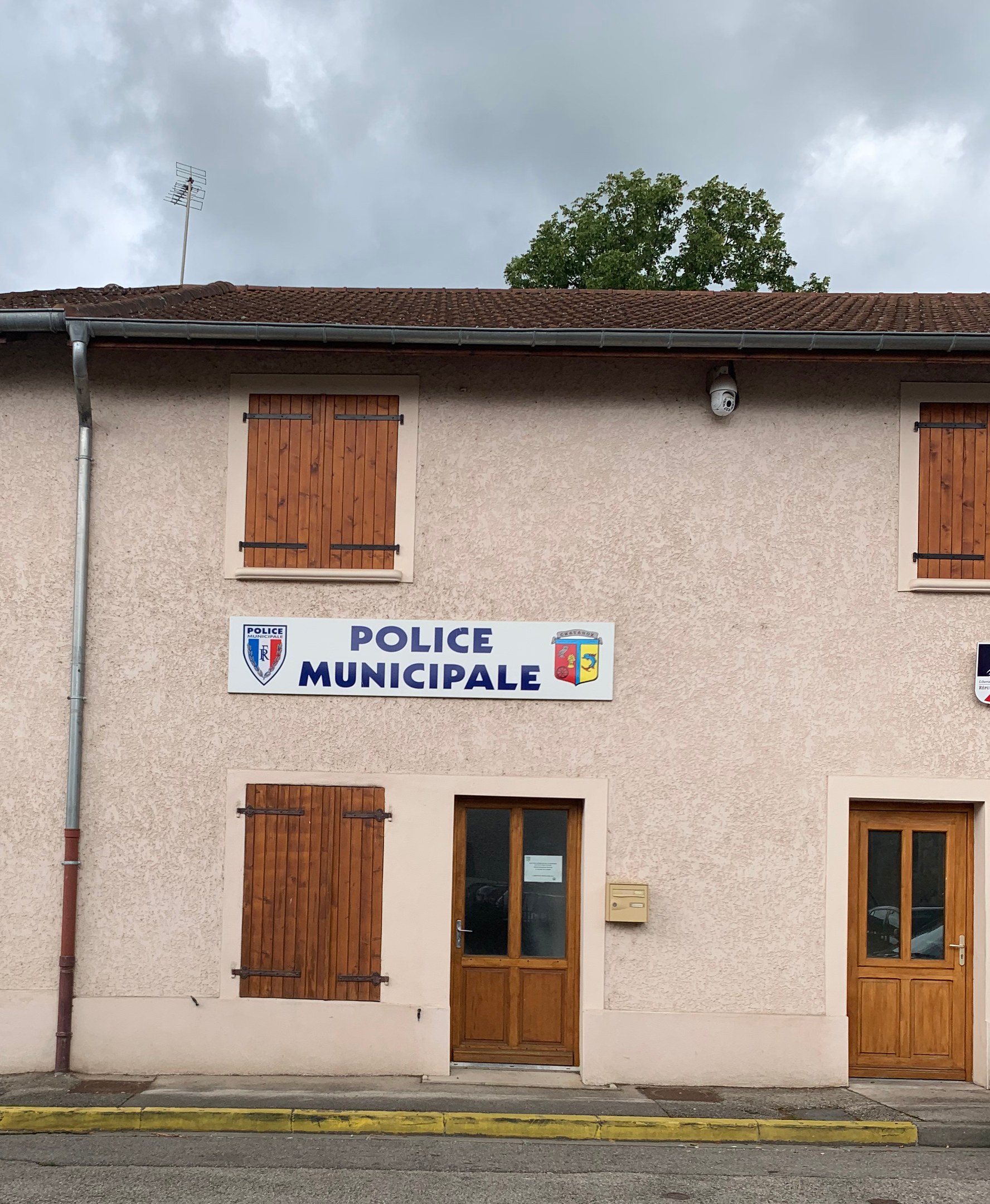 Polizeigebäude mit einem Schild, Fenstern, Türen, einer Namensschild, einer Leitung, einem Baum und einem bewölkten Himmel im Hintergrund.
