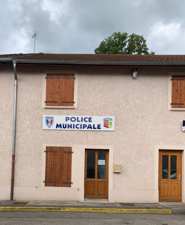 Polizeigebäude mit einem Schild, Fenstern, Türen, einer Namensschild, einer Leitung, einem Baum und einem bewölkten Himmel im Hintergrund.