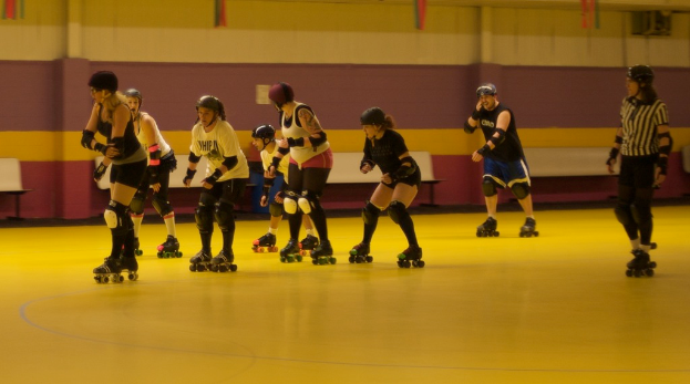 Menschen tragen Kleidung und Schlittschuhlaufen auf einem Boden mit Bänken vor einer Wand.