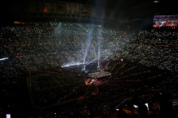 Große Menschenmenge in einem hell erleuchteten Stadion bei Nacht mit einem Bildschirm auf der rechten Seite, der die Ergebnisse der Super Bowl XLVII-Halbzeitshow anzeigt.