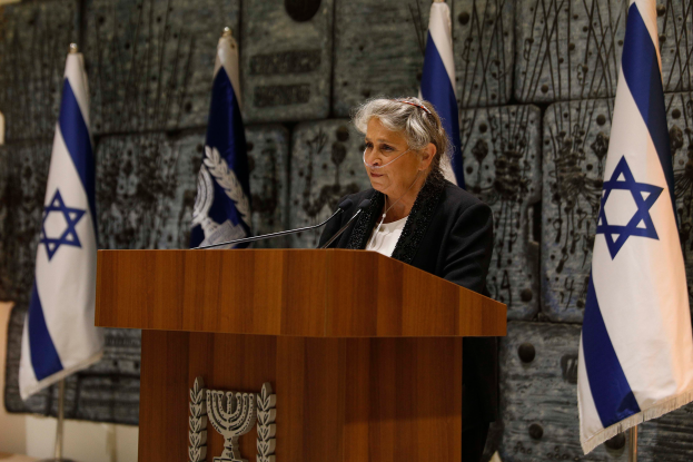 Israeli Premierminister Yitzhak Rabin in einem schwarzen und weißen Kleid vor einem Podium mit mehreren Mikrofonen stehend, während er auf einer Pressekonferenz in Jerusalem spricht, mit israelischen Flaggen und einer Wand im Hintergrund.