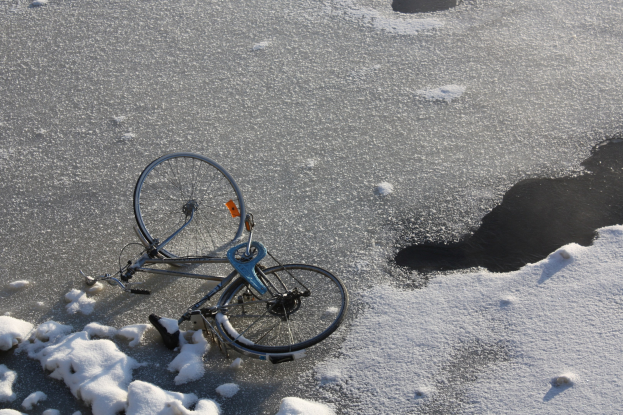 Ein Fahrrad liegt im Schnee neben einer Pfütze Wasser, mit Schnee bedecktem Boden drumherum.