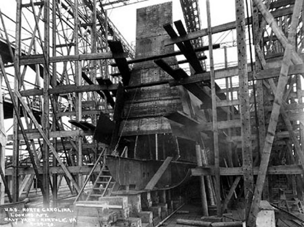 Schwarzes und weißes Foto eines Schiffs in einem Schiffbauwerk, mit hölzernen Pfählen und Treppen im Vordergrund und Himmel im Hintergrund, mit dem Text "Marinebewaffnung" in der linken unteren Ecke.