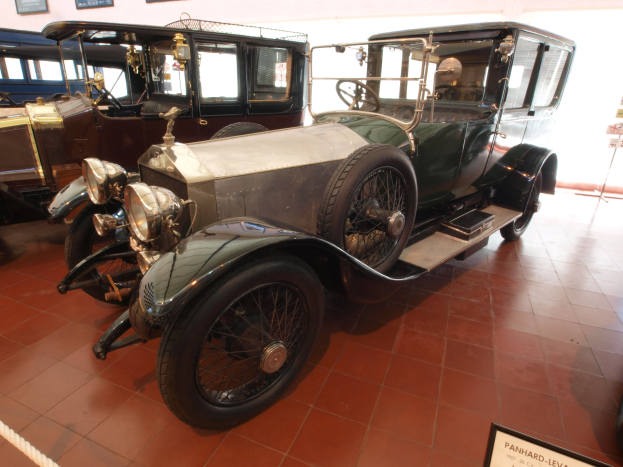 Ein Oldtimer mit schlankem, klassischem Design und glänzender Lackierung ist in einem Museum ausgestellt, umgeben von Informationsschildern, einer Seilabsperrung und gerahmten Gegenständen an der Wand.