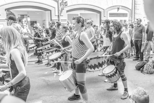 Eine Gruppe von Menschen, die musikalische Instrumente im Freien neben einer geschlossenen Glastür mit einem Licht im Hintergrund spielen.