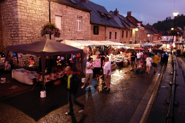 Eine Gruppe von Menschen, die auf der Straße gehen, einige mit Schirmen, Geschäfte mit hängenden Spielzeugen und Taschen, Gebäude mit Fenstern, Bäume, Straßenlaternen und Barrikaden.