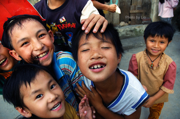 Kinder, die mit einem Grinsen vor einer Straße und einer Wand stehen.