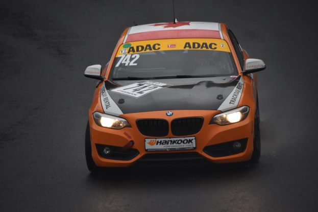 Ein oranges BMW-Rennfahrzeug mit Text und Zahlen auf seiner Karosserie fährt auf einer Rennstrecke.