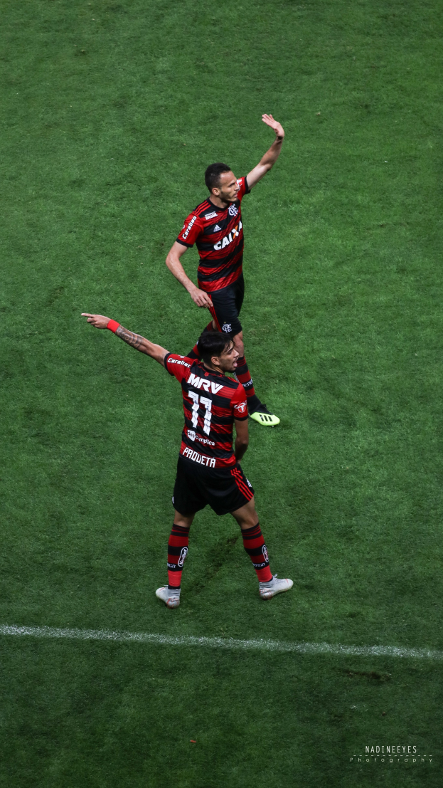 Zwei Fußballspieler in roter und schwarzer Sportbekleidung auf einem saftig grünen Feld.