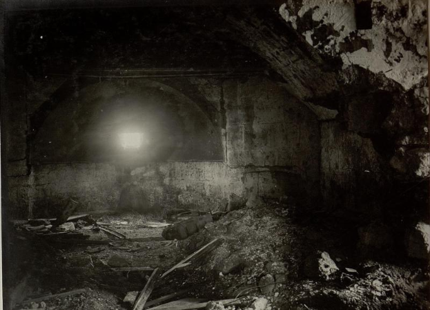 Ein altes Schwarz-Weiß-Foto eines zerfallenden Tunnels mit Schutt auf dem Boden und einer Lampe am Ende, das sich in den Ruinen der Berliner Mauer befindet.
