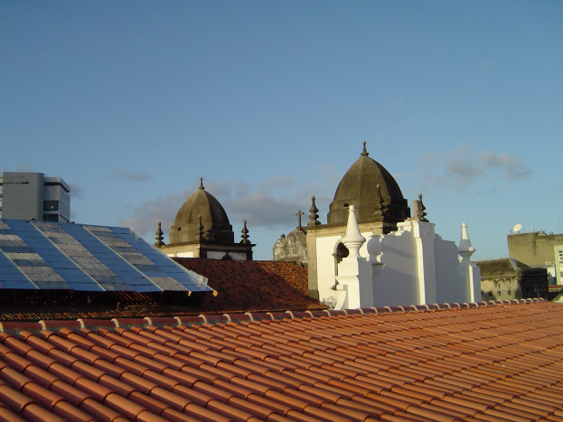 Stadtpanorama mit Gebäuden im Vordergrund, einem blauen Himmel im Hintergrund und Solarpanelen auf einem Dach.