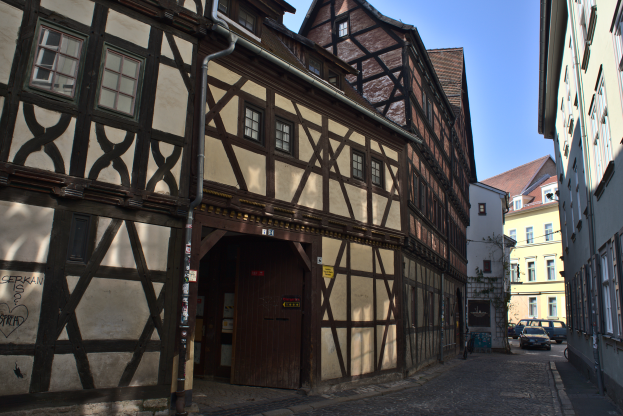 Eine Kopfsteinpflasterstraße in Rothenburg ob der Tauber, Deutschland, gesäumt von Gebäuden auf beiden Seiten, unter einem klaren blauen Himmel mit Fahrzeugen, die die Straße entlangfahren.