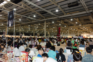 Eine große Gruppe von Menschen versammelte sich um Tische, die mit Büchern, Kartons und anderen Gegenständen gefüllt waren, bei einer Buchmesse.
