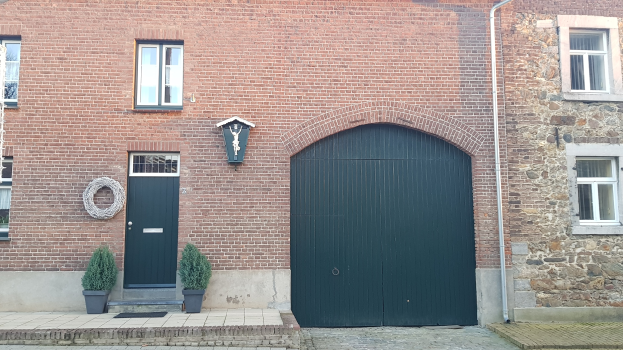 Ein Ziegelgebäude mit einer grünen Tür und Fenstern, eine Leitung an der Seite und Topfpflanzen davor.