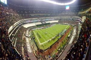 Ein großes Stadion voller Zuschauer, die ein Fußballspiel sehen, mit Spielern und verschiedenen Gegenständen auf dem Feld, beleuchteten Tafeln, Geländern, Bildschirmen und Deckenlampen.