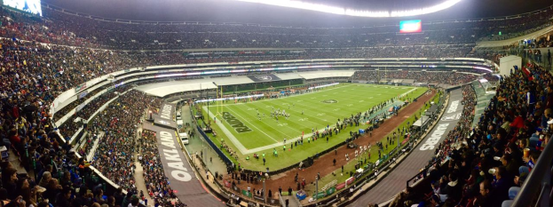 Ein großes Stadion voller Zuschauer, die ein Fußballspiel sehen, mit Spielern und verschiedenen Gegenständen auf dem Feld, beleuchteten Tafeln, Geländern, Bildschirmen und Deckenlampen.