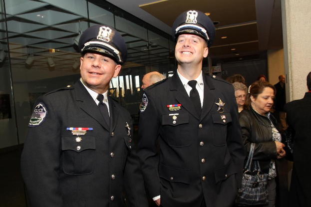 Zwei lächelnde Beamte im Vordergrund, Menschen in der Mitte, Glasfenster links, Lampen und Decke oben und Säulen und Menschen rechts.