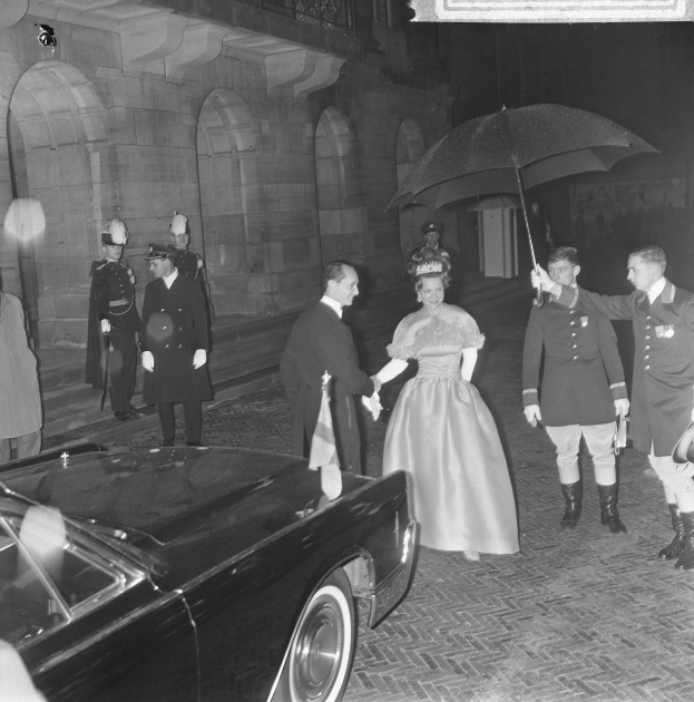 Schwarzes und weißes Foto von Queen Elizabeth II. und Prinz Philip, Duke of Edinburgh, der in förmlicher Kleidung vor Buckingham Palace ankommt, wobei die Queen einen Blumenstrauß und der Duke einen Schirm hält.