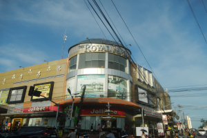 Eine belebte Stadtstraße mit Fahrzeugen, Fußgängern und dem Royal Mall-Einkaufszentrum im Hintergrund.