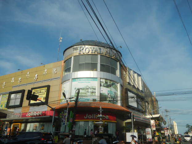 Eine belebte Stadtstraße mit Fahrzeugen, Fußgängern und dem Royal Mall-Einkaufszentrum im Hintergrund.