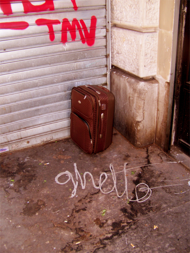 Eine braune Gepäcktasche wird an einer Ecke neben einer Rollladenür in einer unattraktiven Umgebung abgestellt.