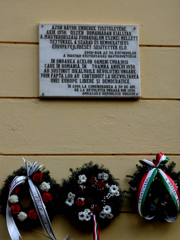 Zwei Kränze mit Bändern hängen an einer Gebäudefassade, über einer Gedenktafel für Holocaust-Opfer.