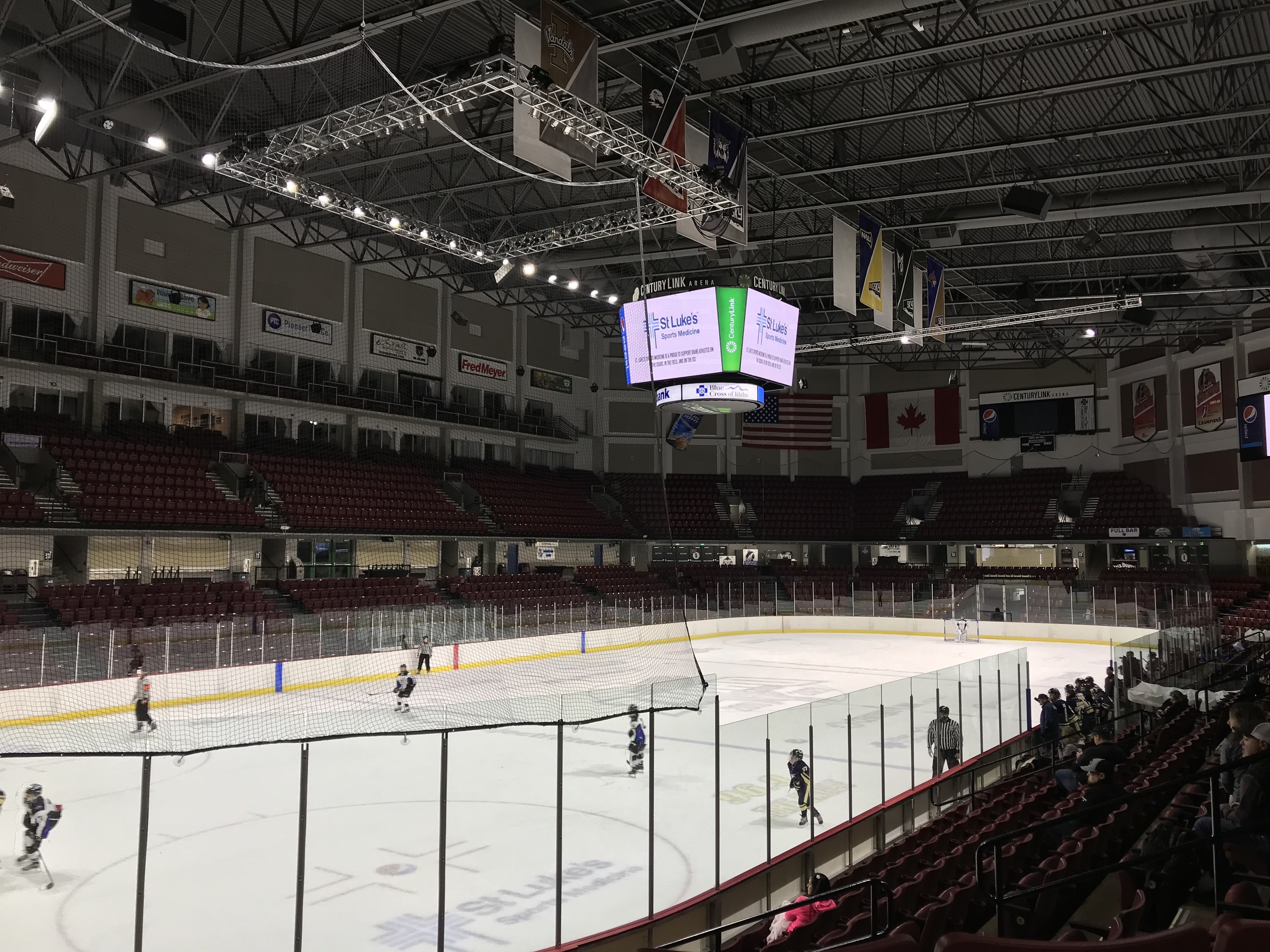 Hockey-Spiel in einer großen Arena mit einem zentralen Netz, Zuschauern auf beiden Seiten, Deckenleuchten und Trägern sowie Bannern an den Wänden, die "St. Louis Blues Arena" beschriftet sind.