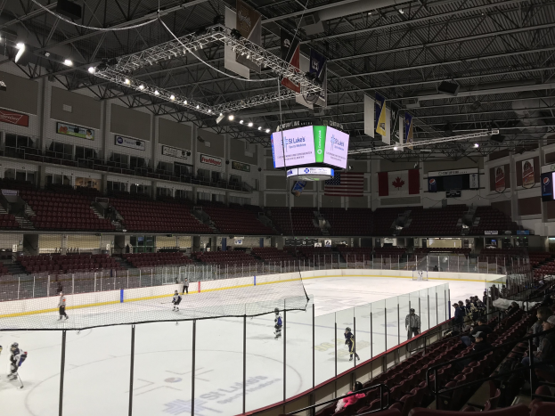 Hockey-Spiel in einer großen Arena mit einem zentralen Netz, Zuschauern auf beiden Seiten, Deckenleuchten und Trägern sowie Bannern an den Wänden, die "St. Louis Blues Arena" beschriftet sind.