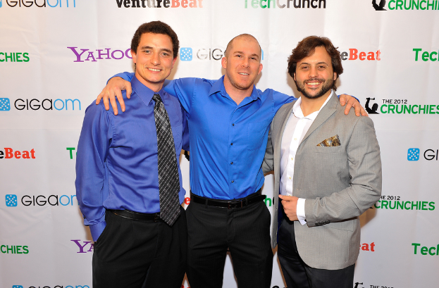 Drei Personen vor einer Sponsoren-Wand, bekleidet.