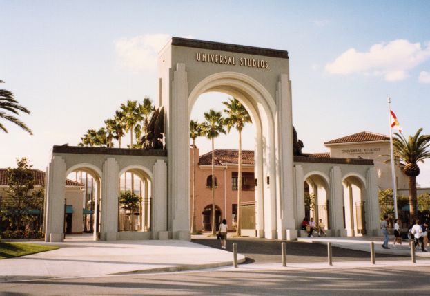 Eingang von Universal Studios Hollywood mit einem Bogen, einer Statue, Menschen, Bäumen, Gebäuden und einem wolkenverhangenen Himmel.