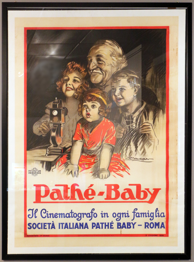 Ein Foto Rahmen an der Wand zeigt ein Poster einer Familie mit dem Text "Pathé-Baby - Il Cinematografico in Ogni Famiglia Società Italiana Pathé Baby - Roma."