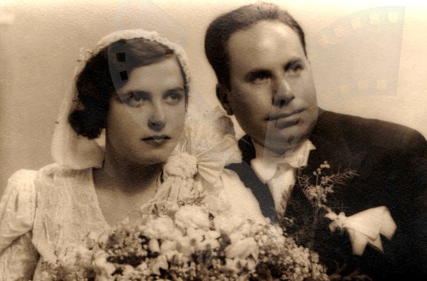 Ein Schwarz-Weiß-Foto eines lachenden Mannes und einer Frau an ihrem Hochzeitstag, die Frau in einem weißen Kleid mit einem Strauß Blumen, der Mann steht neben ihr.