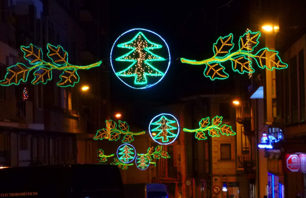 Eine festliche Stadtstraße bei Nacht, dekoriert mit Weihnachtslichtern in Form von Blättern, mit Fahrzeugen, die an Gebäuden auf beiden Seiten vorbeifahren.