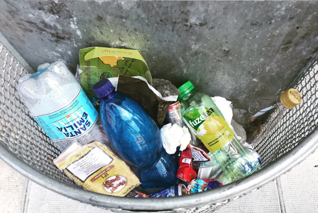 Ein Metallmüllcontainer voller Plastikflaschen, Beutel und anderer Gegenstände.