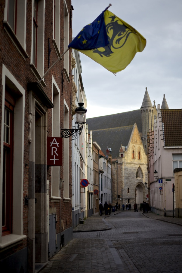 Eine Stadtansicht mit Gebäuden, Menschen auf der Straße, Pfählen, Schildern und einer Flagge auf einem der Gebäude, unter einem Himmel.
